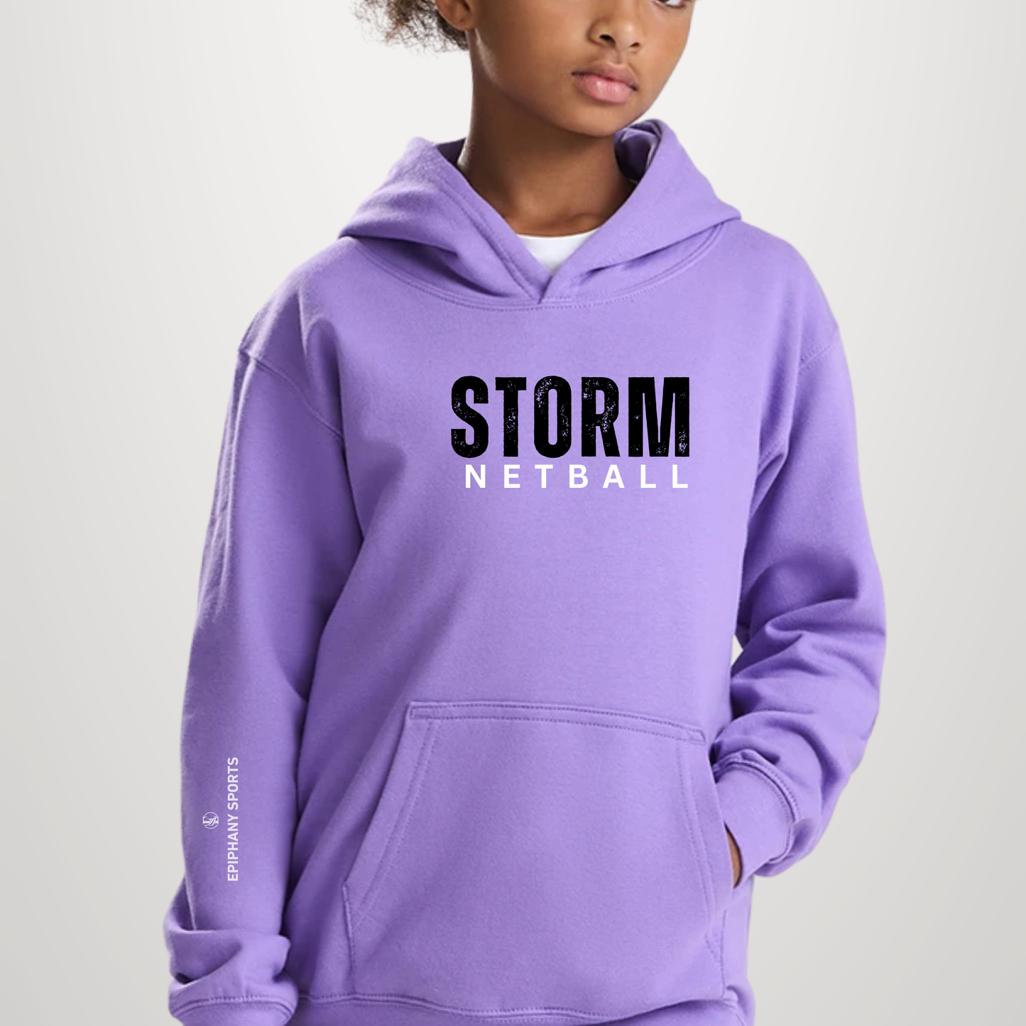 A child wearing a lavender purple hoodie with 'STORM NETBALL' printed in black and white across the chest, and 'STORMLAND SPORTS' on the sleeve, against a light gray studio background.