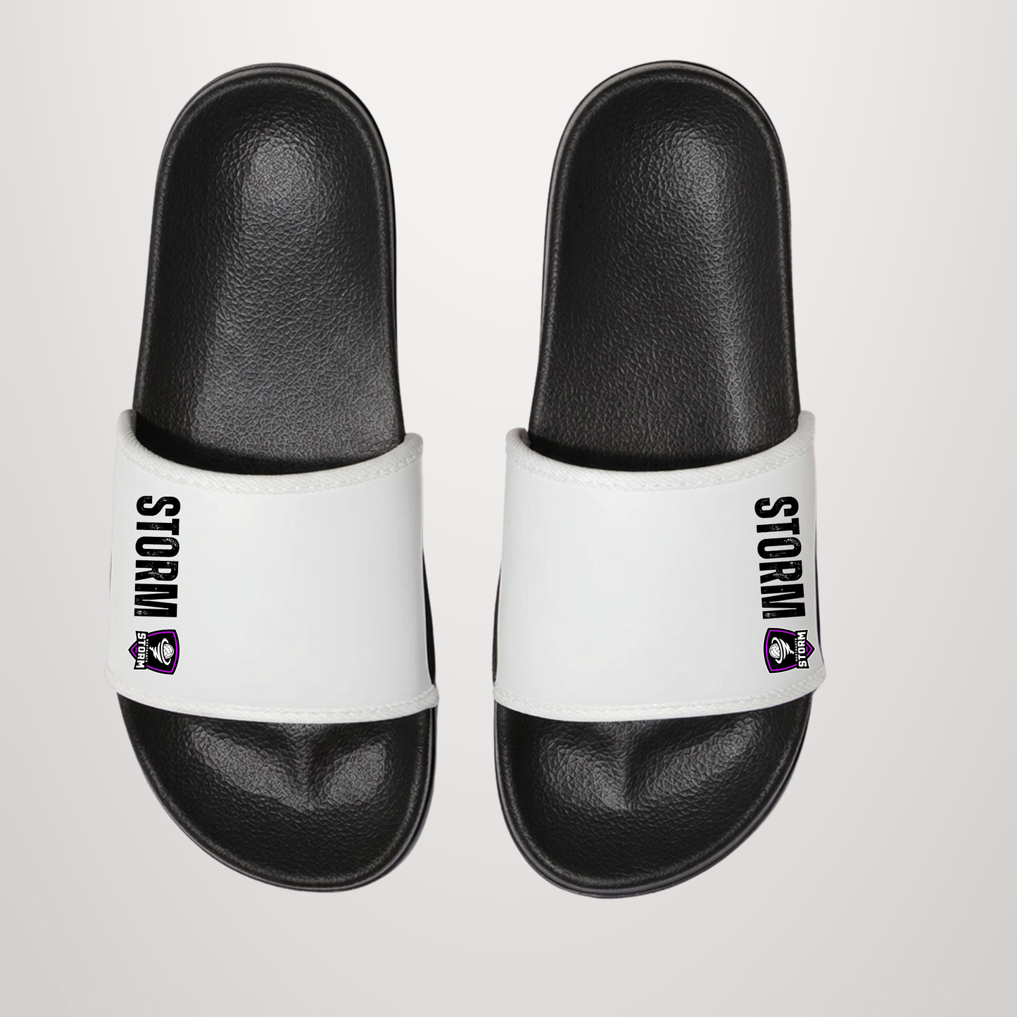 A pair of black and white slide sandals with 'STORM' and a purple mascot logo printed on the white straps, shown from a top-down view on a light gray background.