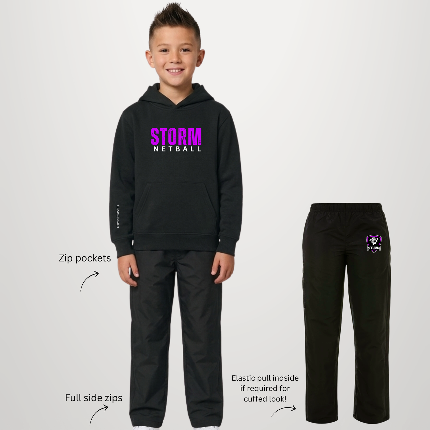 A child model wears a black Storm Netball hoodie and matching black pants against a light gray studio background, with callout text highlighting features like zip pockets and elastic pull inside the pants. A separate flat view of the pants appears on the right with a Storm Netball crest on the left thigh.