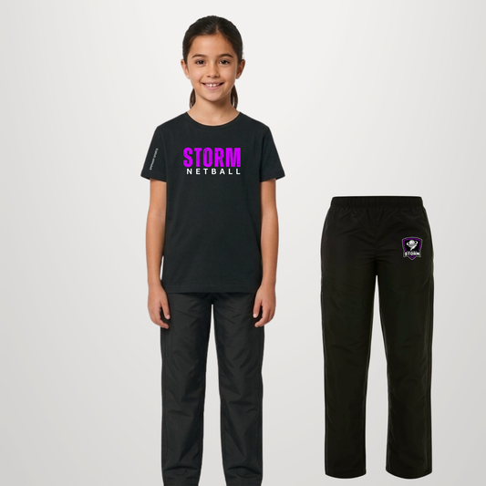 A child model stands wearing a black Storm Netball t-shirt and matching black pants, with the pants shown separately on the right against a light gray studio background.