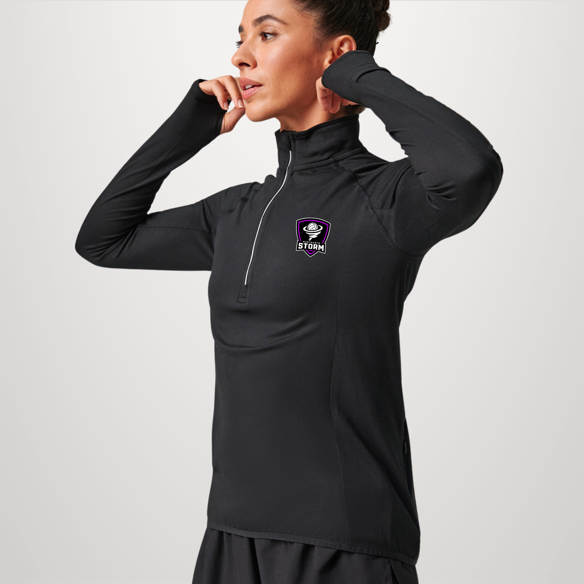 A woman modeling a black long-sleeve athletic quarter-zip pullover with a small purple and white logo on the left chest, set against a plain light gray studio background.