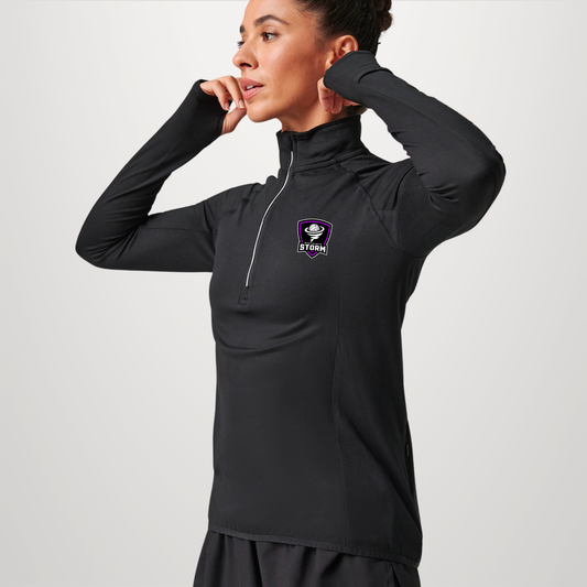 A woman modeling a black long-sleeve athletic quarter-zip pullover with a small purple and white logo on the left chest, set against a plain light gray studio background.