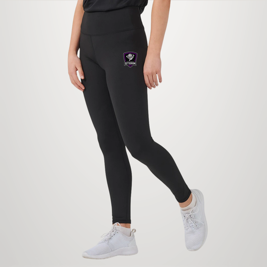 A model wearing black high-waisted leggings with a small purple and white Dri-FIT logo on the left hip, paired with white athletic sneakers, against a light gray studio background.