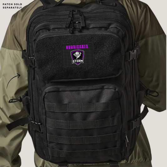 A black tactical backpack shown on a model wearing an olive green jacket. The backpack features a front patch with the text 'HURRICANES by STORM' in purple and white.