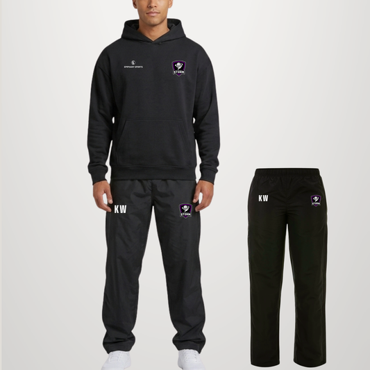 A man modeling a black tracksuit with a matching hoodie and jogger pants, shown against a light gray studio background. The hoodie has a small white logo on the left chest and a purple-and-white crest on the right chest.