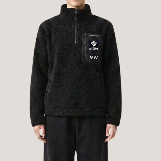 A person wearing a black sherpa fleece quarter-zip pullover with a chest pocket featuring a Storm GW logo patch, paired with black pants, against a light gray studio background.