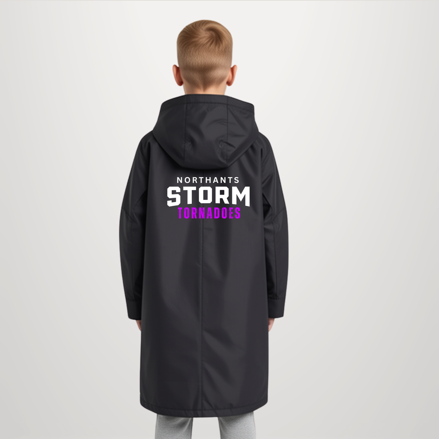 A child viewed from behind wearing a long black hooded jacket with large back text reading 'NORTHANTS STORM TORNADOES' in white and purple, against a light gray studio background.