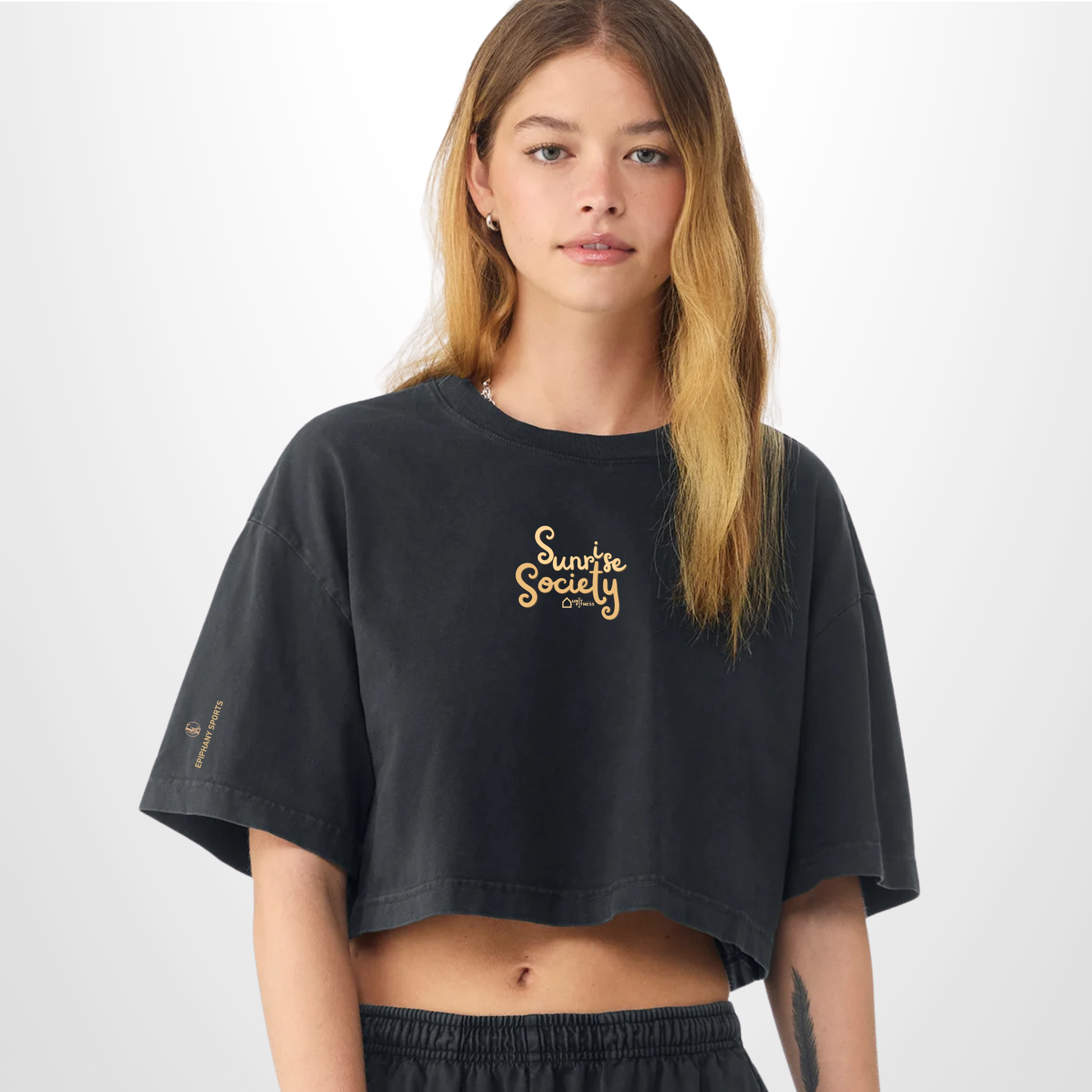 A woman modeling a black cropped t-shirt with a gold 'Sunshine Society' logo on the chest, set against a plain light gray background.