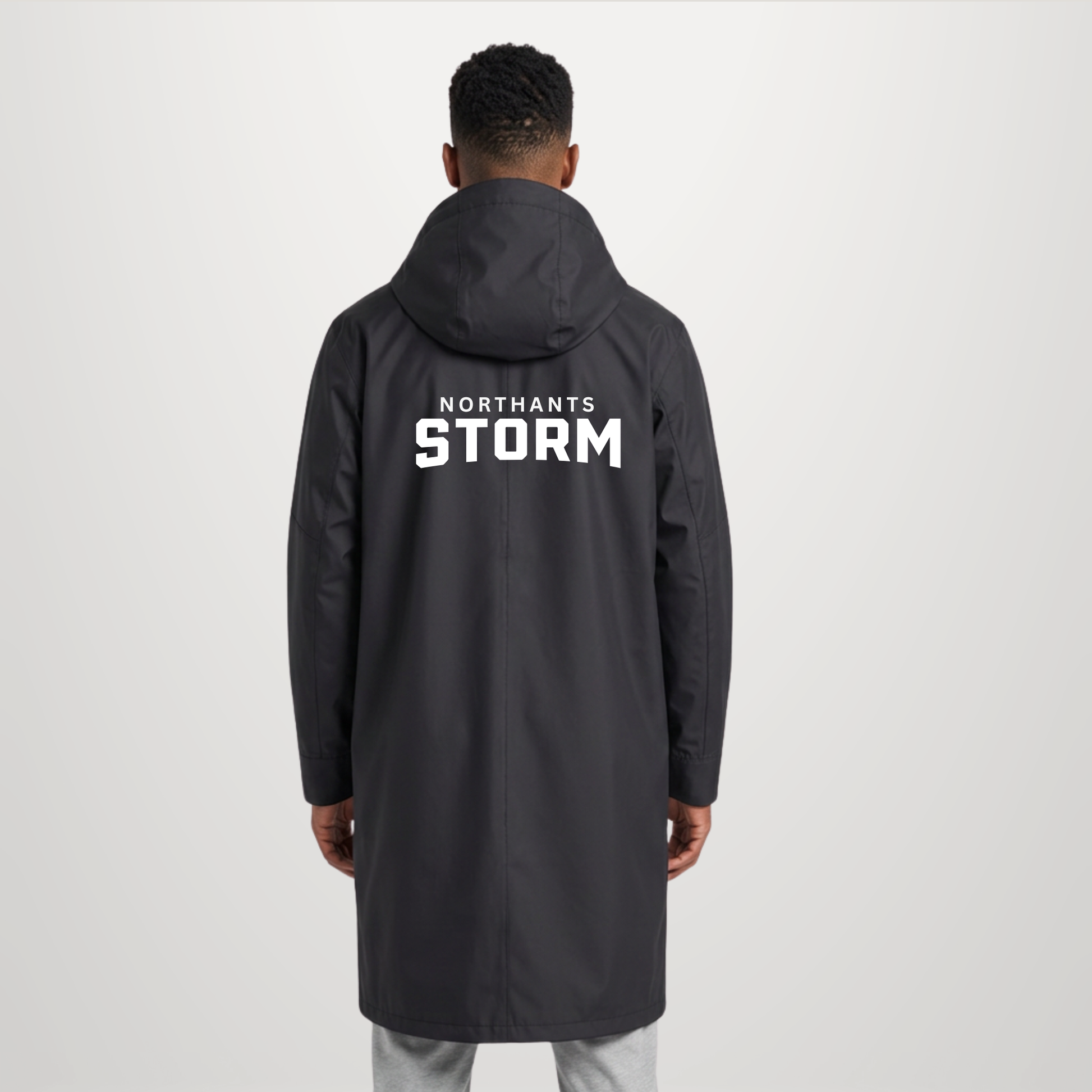 A man viewed from behind wearing a dark gray hooded jacket with 'NORTHANTS STORM' printed in bold white letters on the back, set against a plain light gray studio background.