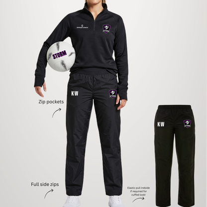 A model wears a black athletic quarter-zip pullover and matching black jogger pants with white and purple team logos, shown on a light gray background with feature callouts and a smaller pants-only view.