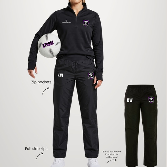 A model wears a black athletic quarter-zip pullover and matching black jogger pants with white and purple team logos, shown on a light gray background with feature callouts and a smaller pants-only view.
